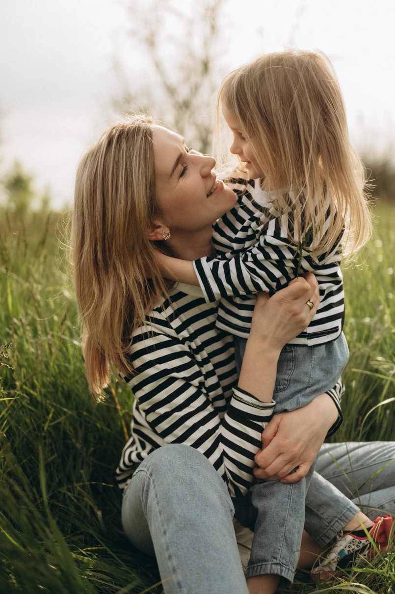 Мама і донька цілуються на траві під сонцем, фотосесія сім'ї на природі.