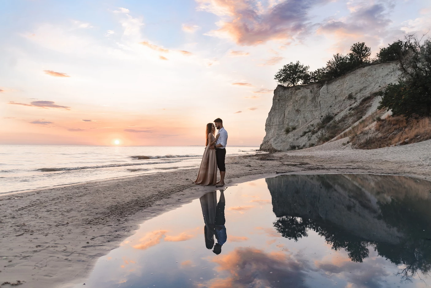 Закохана пара позує на пляжі в Кременчуці під час заходу сонця, їхні відображення блищать у воді.