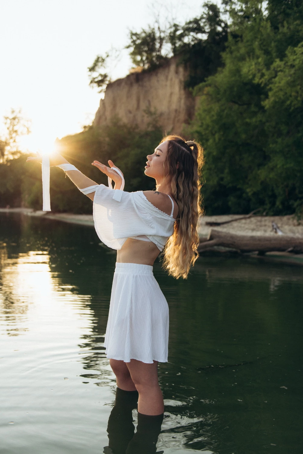 дівчина в білосніжному вбранні знаходиться в річці, з руками, що тримають сонце, передаючи енергію і відчуття життєвої сили, які випромінюються з природи
