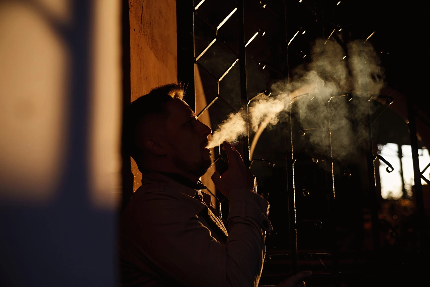 Чарівне фото, на якому чоловік у елегантному костюмі курить, надаючи йому загадковості, тлі заходу сонця