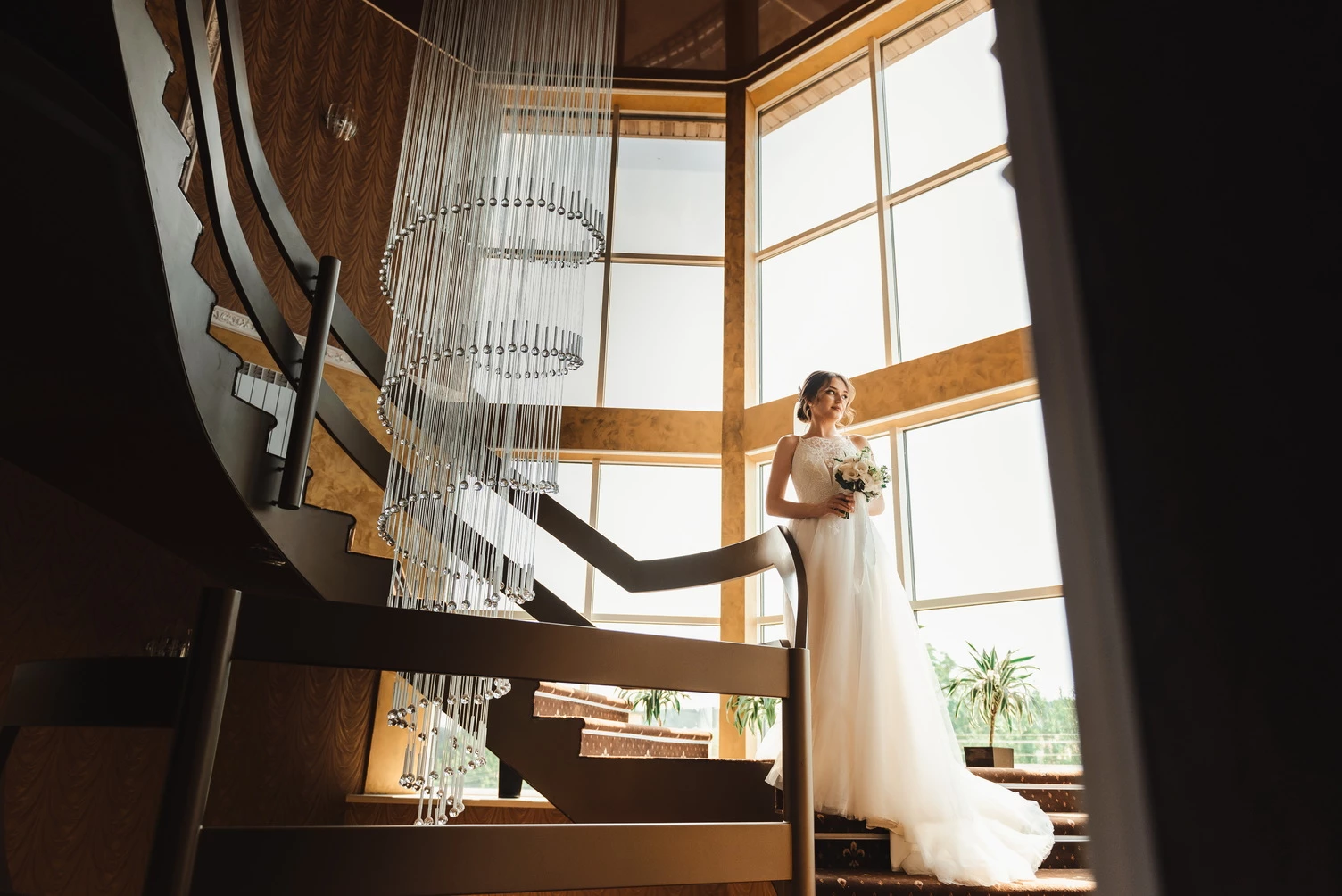 Весільна фотографія з нареченою в шикарній сукні, позуючи на сходах з величезною люстрою в середині, в інтер'єрі з вишуканим дизайном